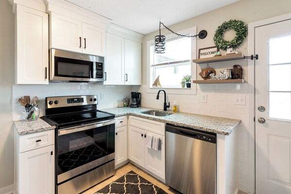 A modern kitchen with white cabinets, stainless steel appliances, a granite countertop, and a black backsplash.