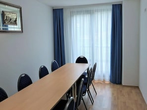 Uma sala de conferência com uma mesa comprida, cadeiras, um quadro emoldurado e uma janela com cortinas.