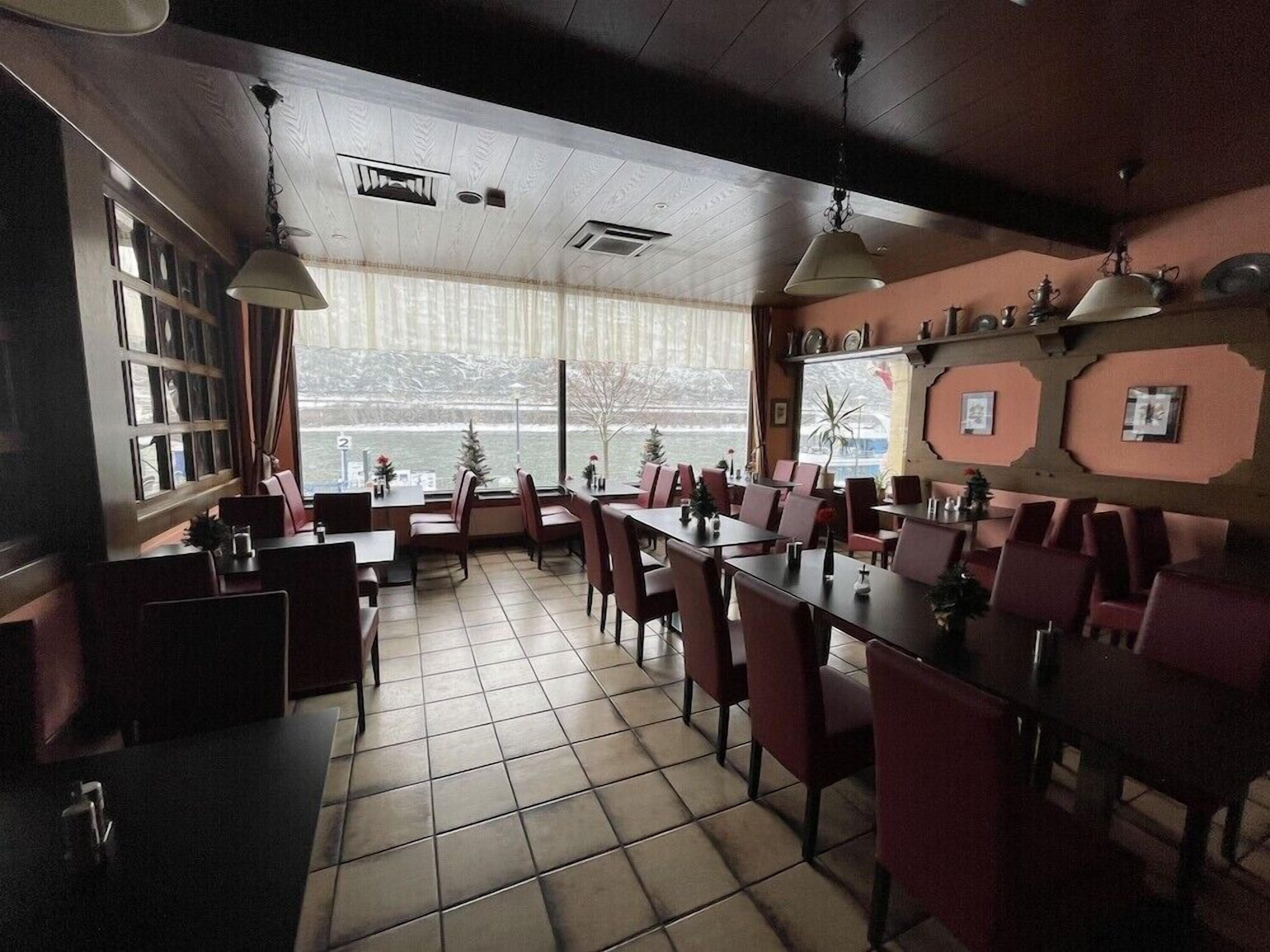 Un restaurante con vistas a un paisaje nevado, mesas y sillas de madera y un suelo de baldosas.