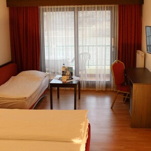 Quarto de hotel com duas camas, uma escrivaninha, uma cadeira e uma mesa com uma garrafa e uma caixa.