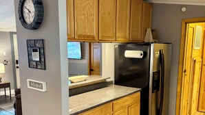 A modern kitchen with wooden cabinets, a stainless steel refrigerator, a clock, and a trash can.