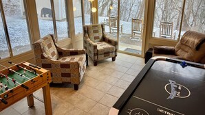 A cozy indoor space with a foosball table, patterned armchairs, and large windows offering a view of the snowy outdoors.
