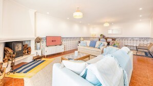 A spacious living room with a fireplace, a sofa set, a television, and a dining area. - Lovely countryside house near the beach (Carvoeira)