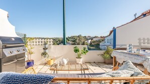 A rooftop terrace with a grill, potted plants, a table set for dining, and a view of the cityscape. - Lovely countryside house near the beach (Carvoeira)