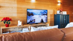 Tunnelmallinen huone, jossa on puuseinä, televisio, josta näkyy lumipeitteinen maisema, punainen maljakko ja sininen kaappi.