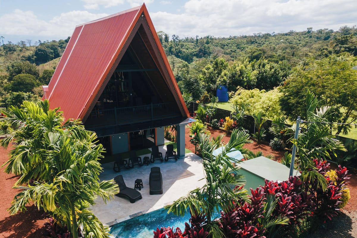 Una villa moderna con techo rojo, piscina y exuberante jardinería tropical.
