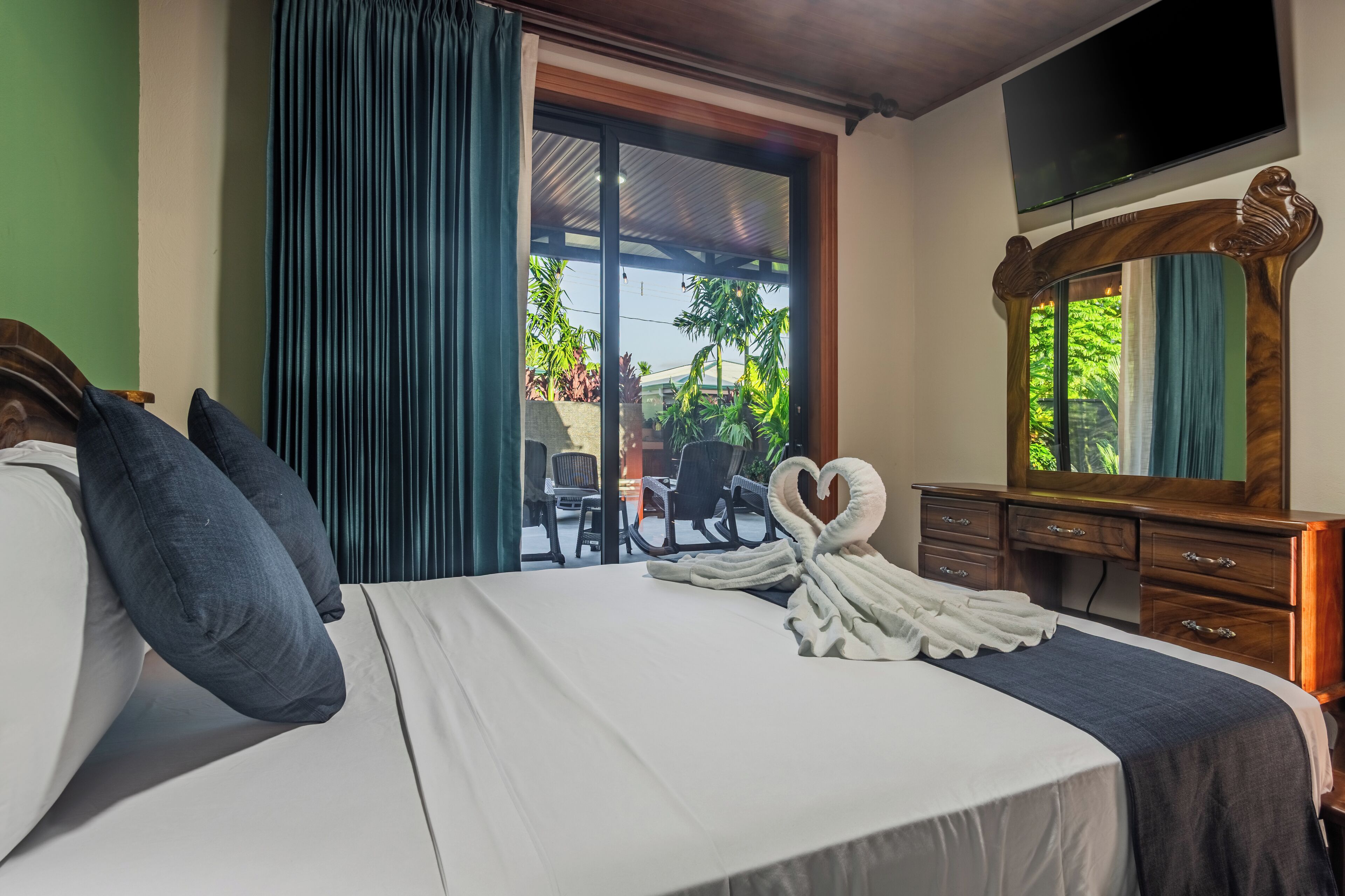A hotel room with a bed, a wooden dresser, a TV, and a view of the outdoors.
