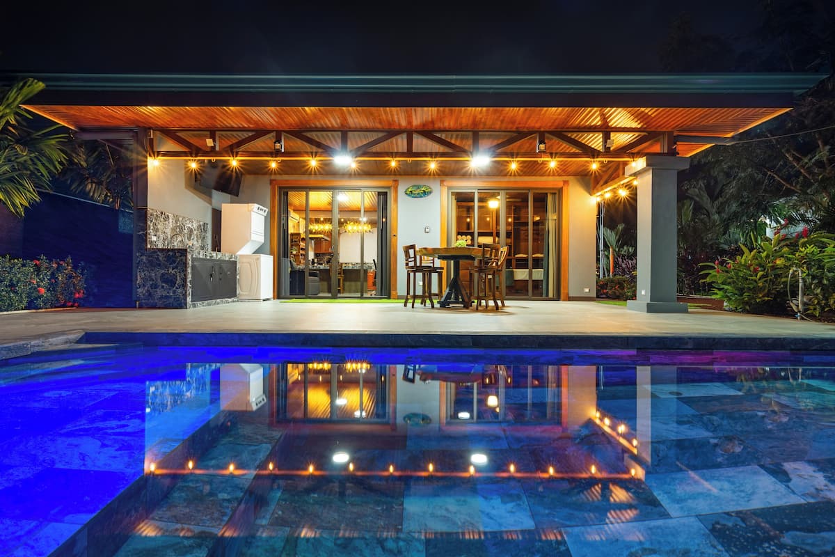 Un área junto a la piscina con un porche cubierto, una mesa de comedor con sillas y vistas a la piscina.