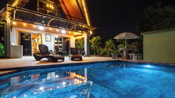 Ein Pool mit Liegestühlen und einer überdachten Terrasse mit Lichterketten.