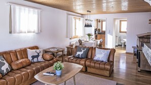 A cozy living room with leather sofas, a coffee table, and a dining area with a kitchen in the background.