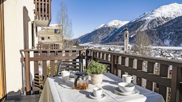 A balcony with a table set for tea, overlooking a snowy mountain landscape.
