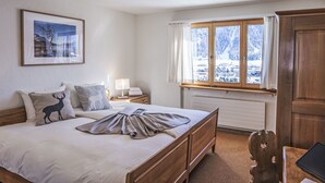 A bedroom with a wooden bed, a nightstand with a lamp, a window with curtains, a radiator, and a framed picture on the wall.