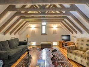 Ein Loft-Zimmer mit freiliegenden Holzbalken, einer Couch, einem gemusterten Teppich, einem Fernseher und einem Bücherregal.