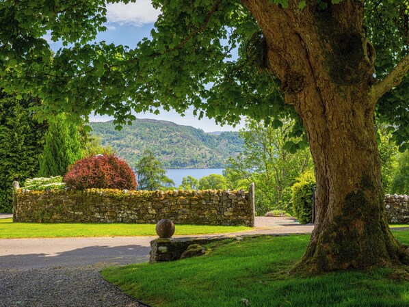 Eine Steinsäule, ein großer Baum und Blick auf einen See und Hügel.