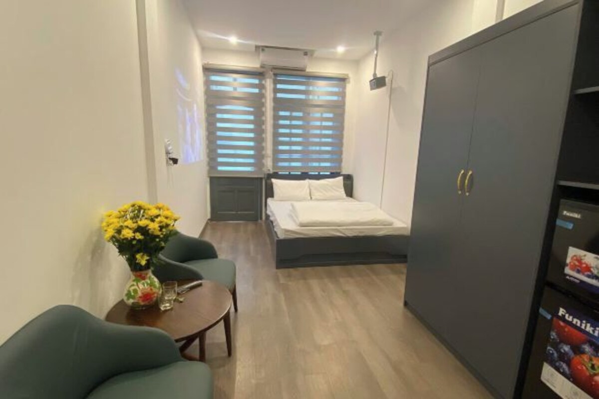 Un dormitorio compacto con cama, armario, una pequeña mesa con un florero y una silla.