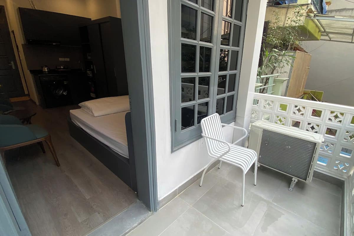 Een balkon met een witte stoel, een bed en een raam met uitzicht op een tuin.