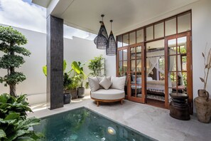 A modern outdoor pool area with a sofa, potted plants, and a wooden door leading to a bedroom. - Plawa Laguna Bali (Pererenan)