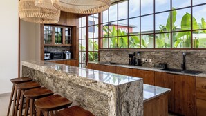 A kitchen with a large island, bar stools, and hanging wicker chandeliers. - Plawa Laguna Bali (Pererenan)