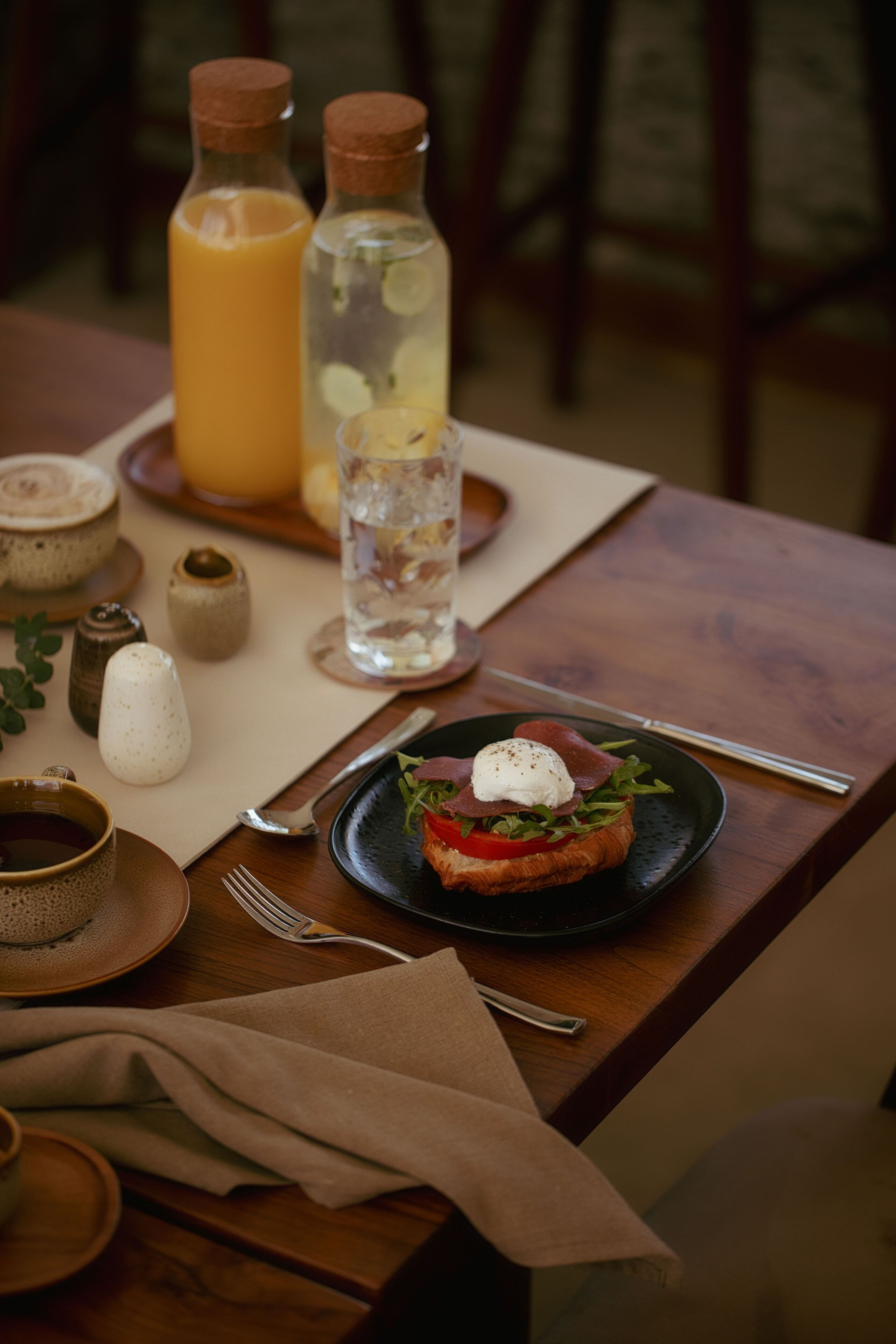 Ein Holztisch mit einem Teller Essen, einem Glas Wasser und zwei Saftflaschen.