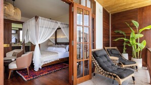 Un dormitorio con cama, una zona de estar con sillas, un ventanal grande y una planta en maceta.
