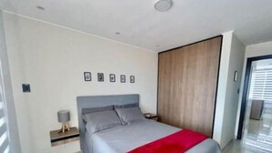 Une chambre à coucher moderne avec un lit, une table de chevet, une lampe et une armoire.