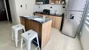 Une cuisine moderne dotée d’un îlot central, de deux tabourets blancs, d’un réfrigérateur en acier inoxydable et d’un four à micro-ondes.