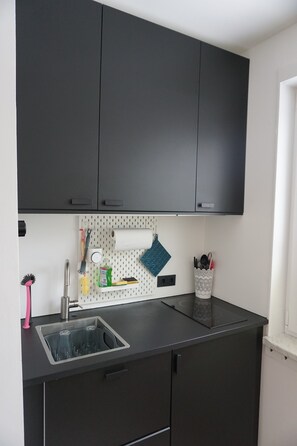 A kitchen with dark cabinets, a stainless steel sink, and a pegboard with kitchen utensils. - Apartment 'Muggelbude' with Mountain View, Shared Garden and Wi-Fi (Braunlage)