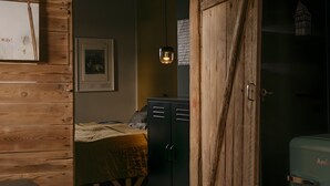 Een kamer met houten wanden, een bed met quilt, een bureau, een kledingkast en een groen apparaat.