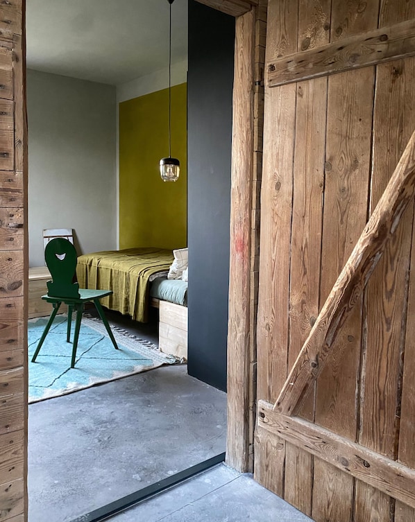 Una habitación con una cama, una silla verde y una lámpara colgante.