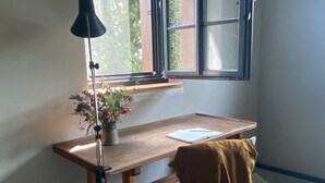 Een hoekappartement met een houten bureau, een raam, een lamp, een stoel en een plant in pot.