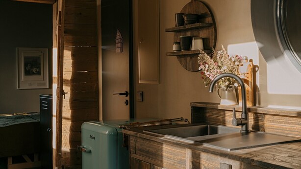 Een keuken met houten kastjes, een spoelbak, een vintage blauwe koelkast en een wandplank met keukengerei.