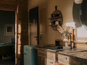 Una cocina con armarios de madera, un lavamanos, un refrigerador azul antiguo y una repisa con utensilios de cocina.