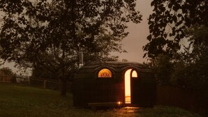 A small, rustic wooden structure with an arched entrance, surrounded by trees and a grassy area. - Holiday Home 'Stall Und Sterne' with Mountain View, Shared Terrace and Wi-Fi (Hirschfeld)