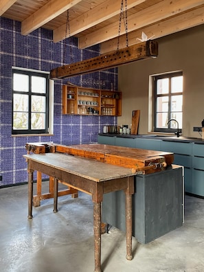 Une cuisine avec une grande table en bois, un plan de travail bleu à motifs et une fenêtre.