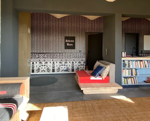 A room with a patterned wall, a red sofa, a bookshelf, and a small table.
