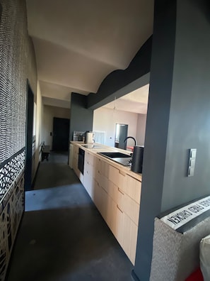A narrow hallway leading to a kitchen with a sink, cabinets, and a microwave.