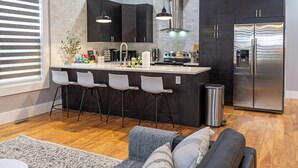Een moderne keuken met donkere kasten, een roestvrijstalen koelkast en een bar met witte stoelen.