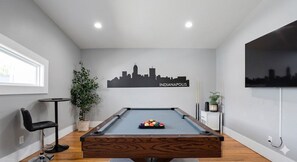 A pool table with a city skyline decal, a potted plant, and a television on the wall. - Stylish 4BR 3K sqft Beauty walking distance to Fountain Square (Indianapolis)