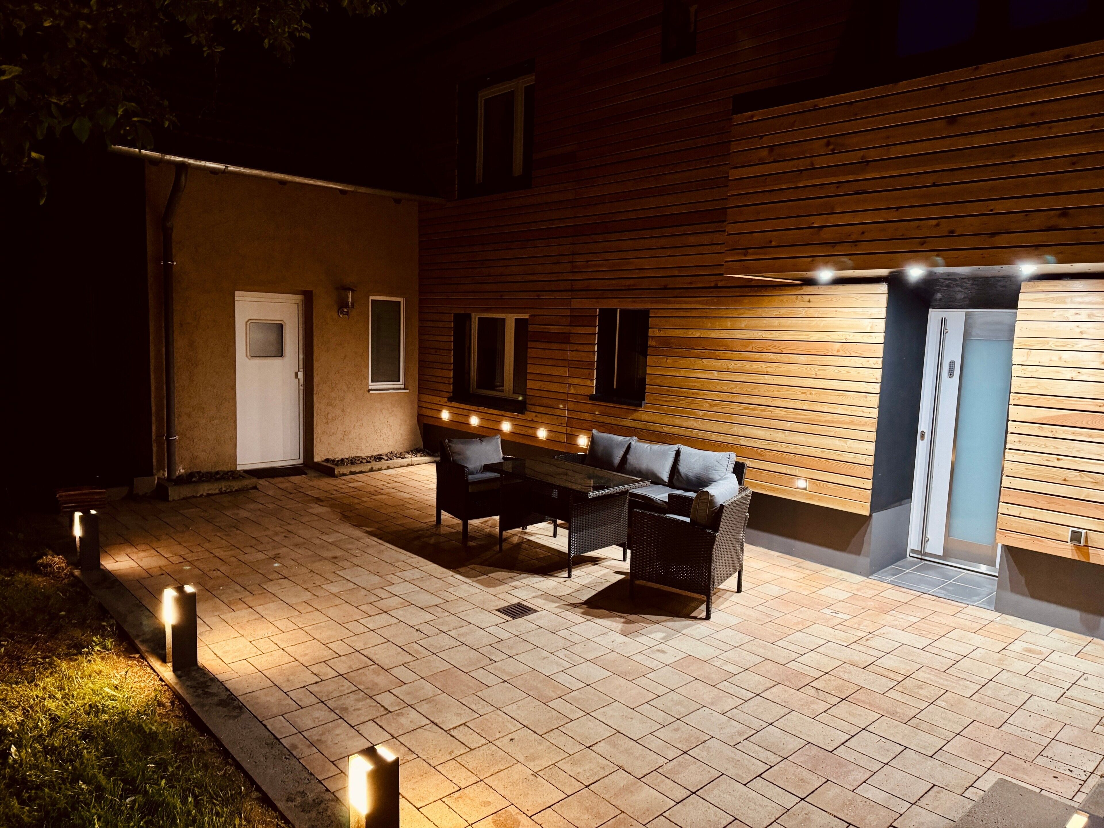An outdoor patio with a table and chairs, a door, and a wall with windows.