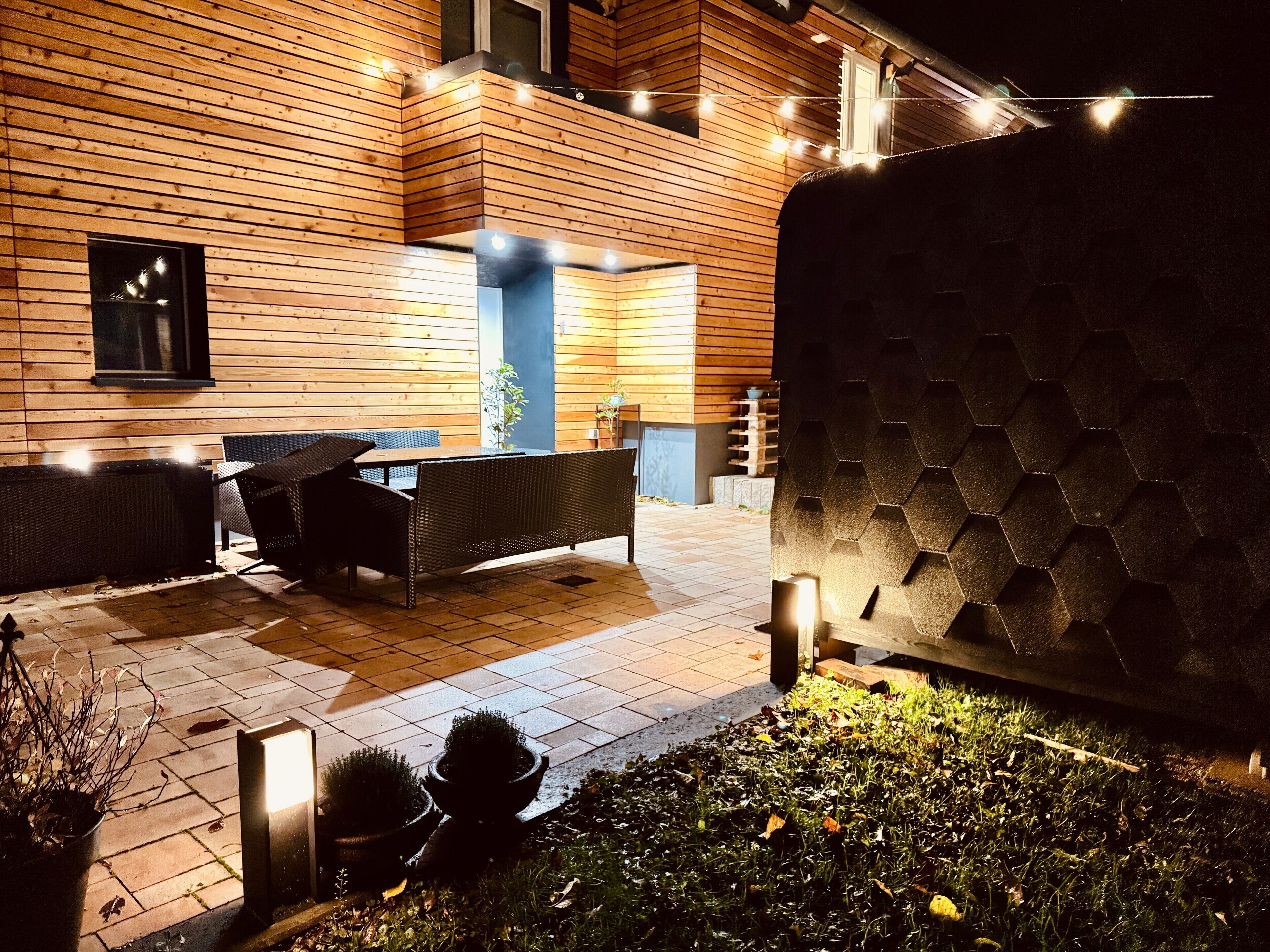 An outdoor patio area with wooden walls, a table with chairs, and string lights.
