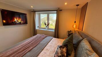 Une chambre à coucher avec un lit, une cheminée, une fenêtre avec des rideaux et un luminaire suspendu.