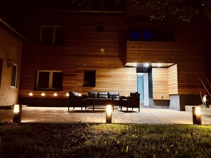 Un bâtiment moderne avec une façade en bois, un espace extérieur aménagé pour s’asseoir et une porte bleue.