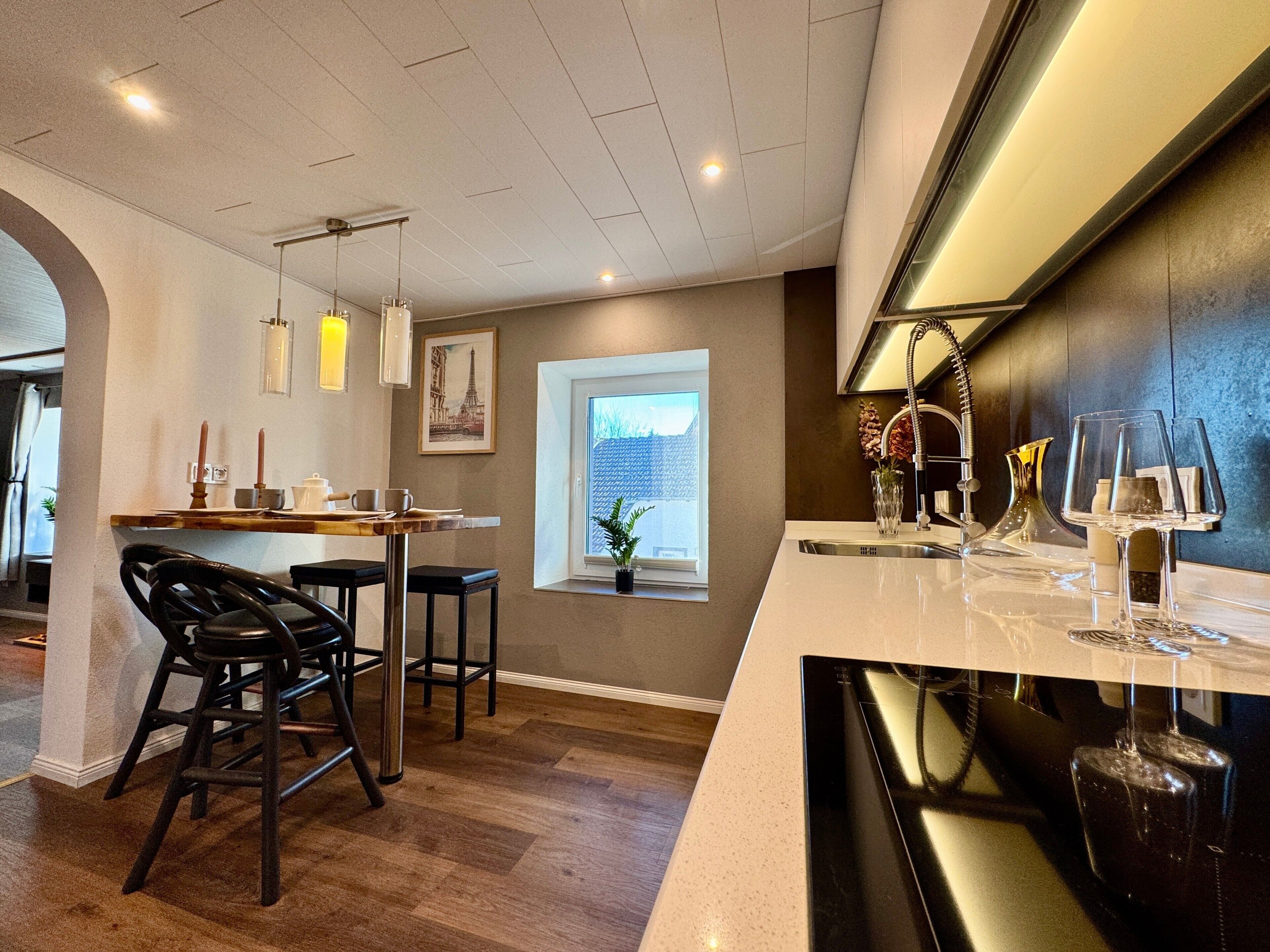 Cozinha moderna com área de bar, piso de madeira e iluminação pendente.