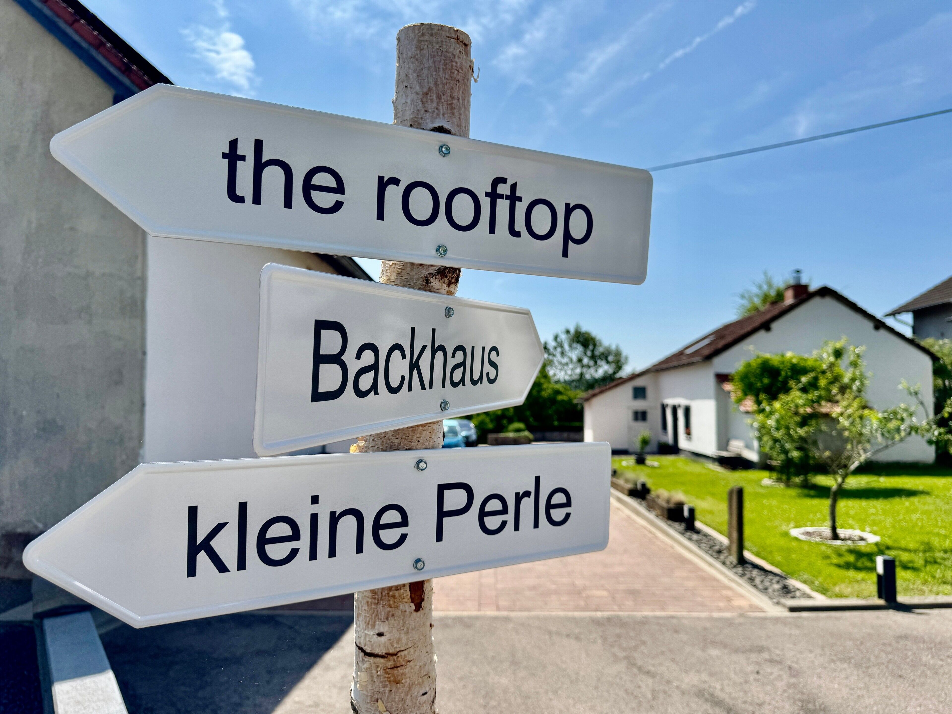 Un cartello direzionale con frecce che indicano 'il rooftop', 'Backhaus' e 'kleine Perle'.