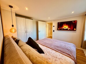 Une chambre à coucher avec un lit, une armoire, un tableau représentant un feu et un luminaire suspendu.