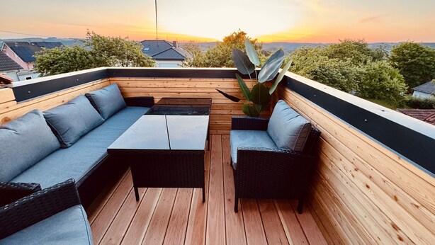 An outdoor seating area with a wooden deck, a sofa, a table, and a potted plant. - Apartment 'The Rooftop Of Lot54' with Private Terrace, Private Garden and Wi-Fi (Feuerscheid)