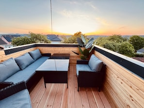 Uma área externa com assento, deck de madeira, sofá, mesa e um vaso de planta.