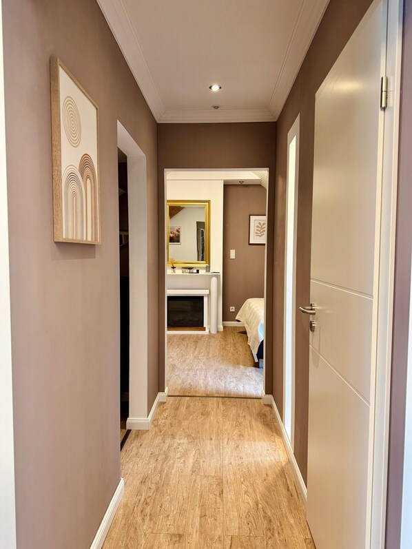 Un couloir avec un plancher en bois, une porte sur la droite et un miroir sur la gauche.