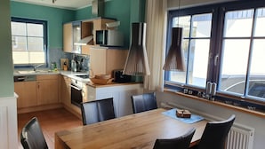 A compact kitchen with a dining area, a microwave, a kettle, and a window with curtains. - 'Haus Windroos' with Private Terrace, Garden, and Wi-Fi (Zingst)