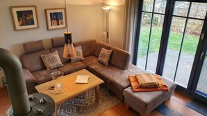 A modern living room with a sectional sofa, a coffee table, a lamp, and a view through a glass door. - 'Haus Windroos' with Private Terrace, Garden, and Wi-Fi (Zingst)